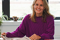 A woman sits at a table and smiles at the camera