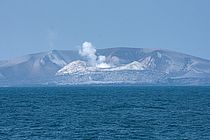[Translate to English:] Ein rauchender eingestürzter Vulkankegel im Meer