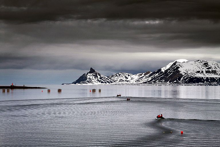 Dunkle Wolken hängen über den Kongsfjord Spitzbergen, in dem rote Versuchsanlagen liegen.