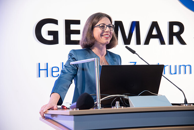 Eine dunkelhaarige Frau im blauen Blazer steht an einem Rednerpult, im Hintergrund ist das Logo "GEOMAR" zu sehen.