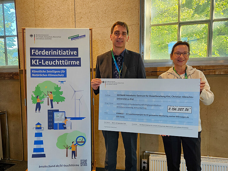 Ein Mann und eine Frau halten einen großen symbolischen Scheck in den Händen