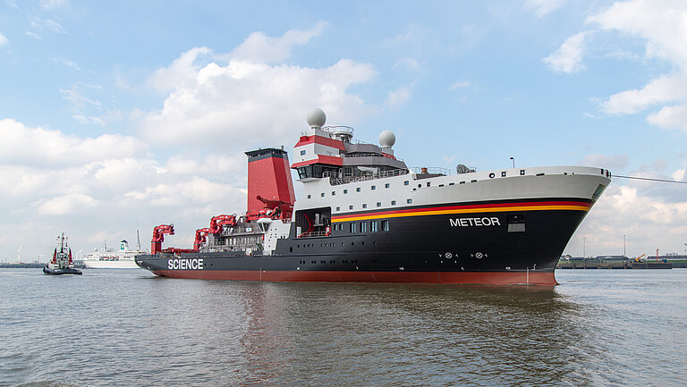 Ein großes Schiff mit schwarz-rotem Rumpf und weißen Aufbauten wird an einer Trosse über das Wasser geschleppt.