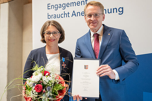 Eine Frau mit Blumenstraß und ein Mann mit Urkunde lächeln in die Kamera