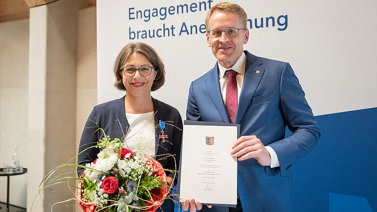 Eine Frau mit Blumenstraß und ein Mann mit Urkunde lächeln in die Kamera