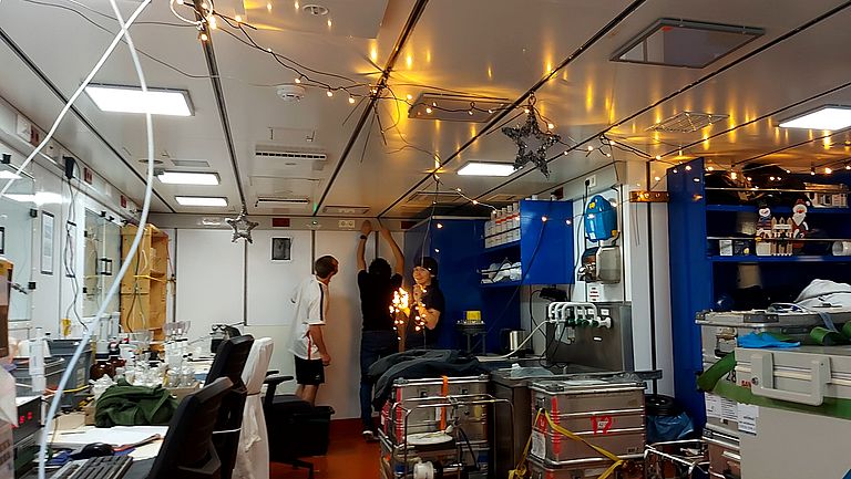 In a laboratory aboard a ship, fairy lights and stars are being hung up.