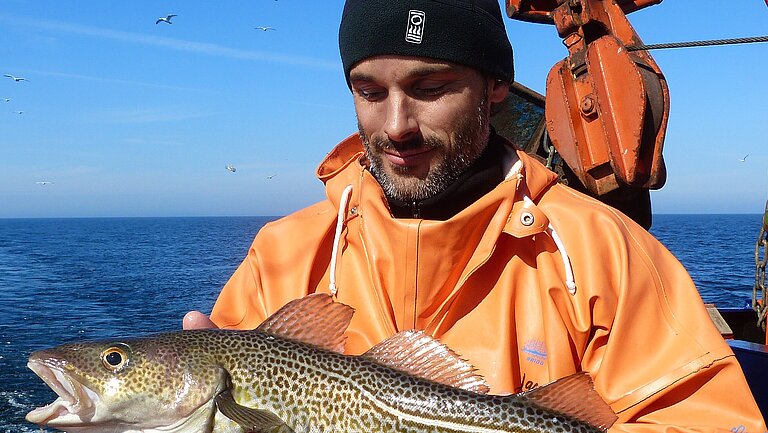 Ein Mann im Ölzeug mit einem Fisch in der Hand