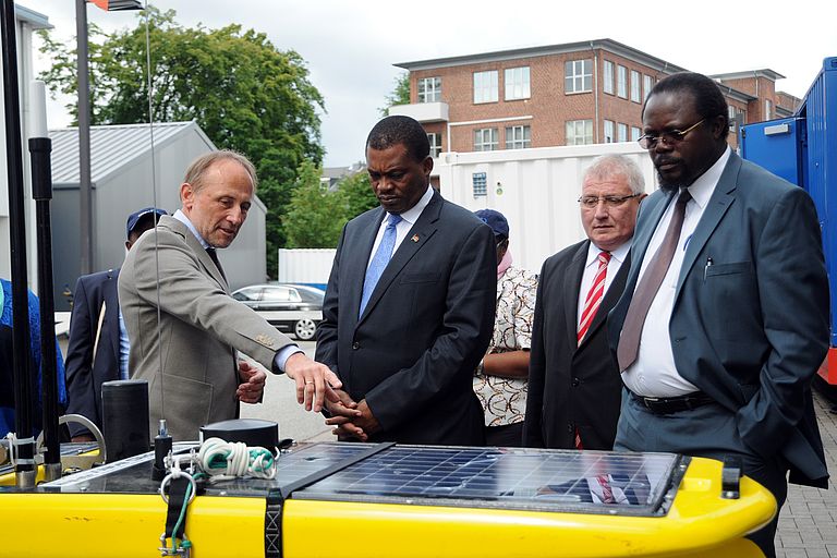 Leiter des Technik- und Logistikzentrums, Dr. Peter Linke (l), erläutert dem Sprecher der kenianischen Nationalversammlung, Hon. Justin B. N. Muturi (m) und dem schleswig-holsteinischen Landtagspräsidenten Klaus Schlie (2.v.r.) einen Waveglider. Foto: Jan Steffen, GEOMAR.