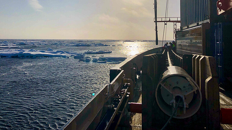 View across the deck of a research vessel onto the sea, where ice floes are floating