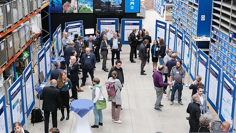 A large hall with poster walls, people in conversation among them.
