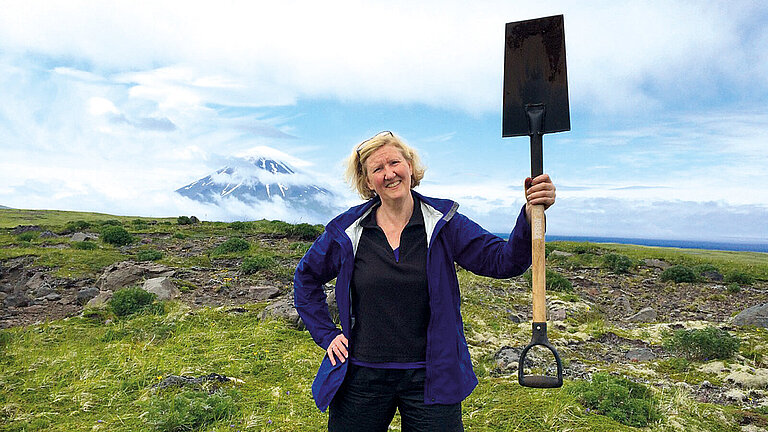 A woman in the countryside holds up a spade