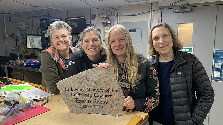 Vier Forscher:innen stehen an einem Tisch und präsentieren den Gedenkstein für Professor Dr. Erwin Suess