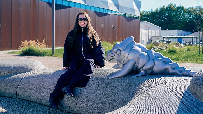 Künsterlin Mary-Audrey Ramirez sitzt auf ihrem Kunstwerk vor dem Gebäude des GEOMAR
