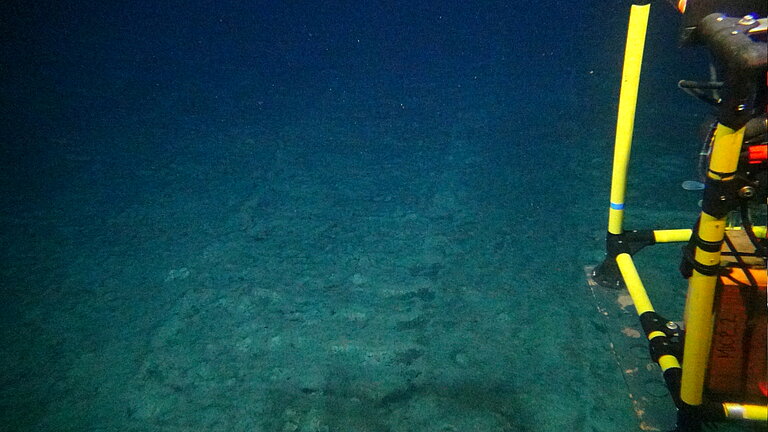 Image from the deep sea: traces in the sediment and, on the right-hand edge of the picture, a yellow measuring instrument