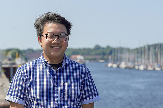 A photo of Jeng Hann Chong standing in front of a body of water.
