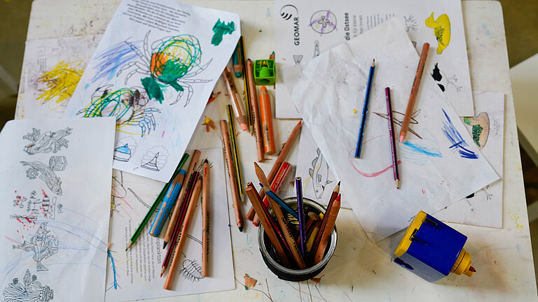 Coloured-in sheets of paper and coloured pencils are lying on a small table