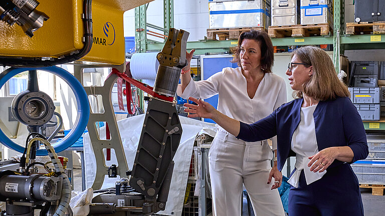 Zwei Frauen in eleganten Hosenanzügen schauen sich einen Unterwasserroboter an.