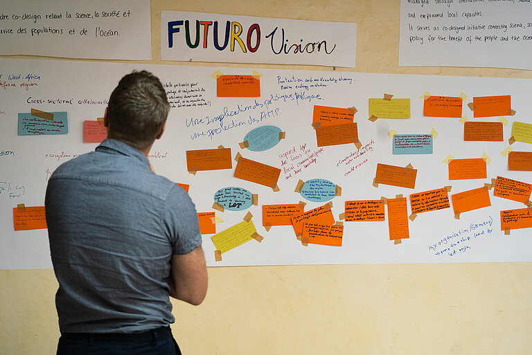 A man stands in front of a pinboard with colourful notes. 