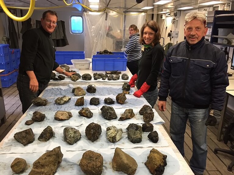 Researchers are standing next to a table on which numerous rock samples are laid out.