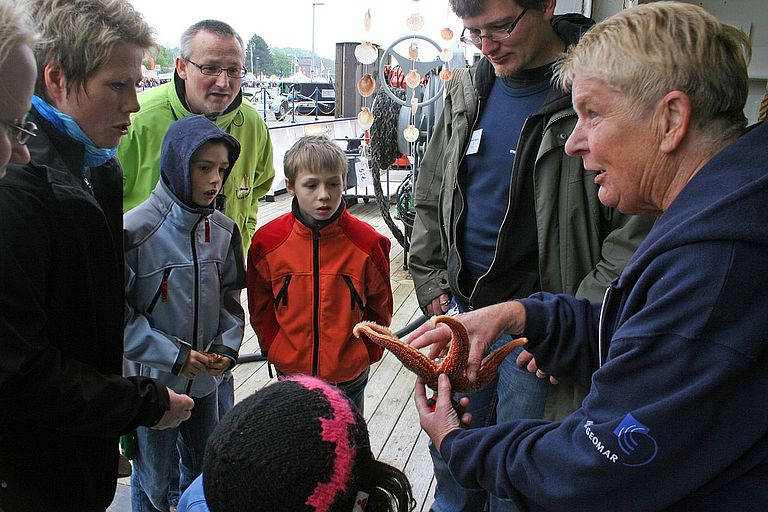IFM-GEOMAR Mitarbeiterin Heidi Gonschior (Mitte) mit einem großen Seestern aus dem Kattegat und einem kleinen aus der Kieler Förde umringt von kleinen Meeresforschern.