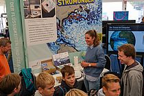 Schulkinder und Studierende vor einem bunten Poster mit der Aufschrift "Meeresströmungen"
