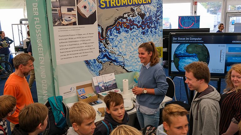 Schulkinder und Studierende vor einem bunten Poster mit der Aufschrift "Meeresströmungen"