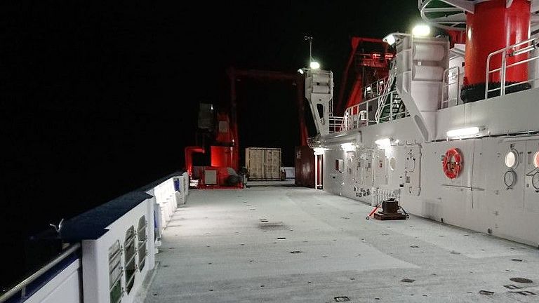 Snow covers the deck of a research vessel at night.