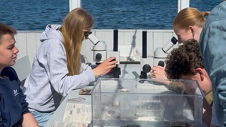 Four teenagers are sitting around a table; two are looking through binoculars