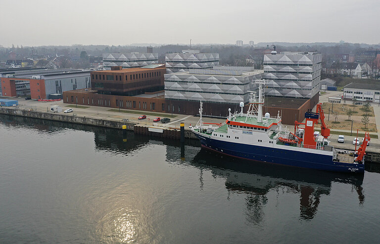 Gebäude an einem Fluss mit Forschungsschiff im Vordergrund