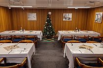 Ein geschmückter Tannenbaum und vier gedeckte Tische in der niedrigen Messe an Bord eines Schiffes