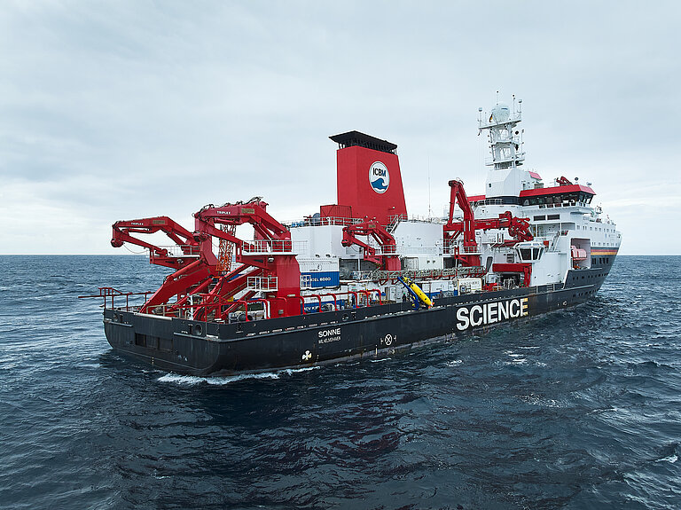 A black-and-white research vessel with a red funnel and a crane at sea