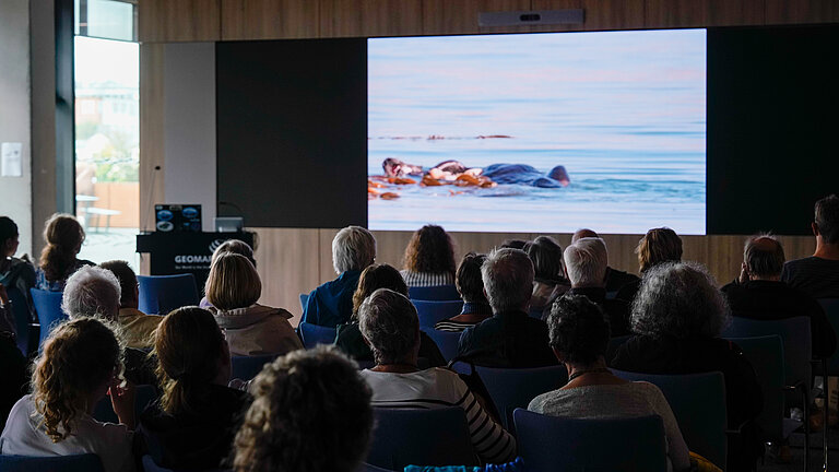 Large conference hall; a film about mussels is being shown on the screen at the front
