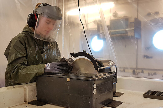 An Bord der METEOR durchtrennt eine Wissenschaftlerin eine Gesteinsprobe mit der Kreissäge. Sie trägt Gehörschutz und einen Gesichtsschild.