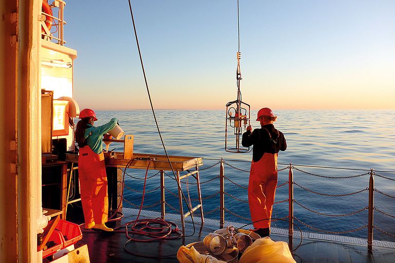 A man and a woman in working clothes stand on the deck of the research vessel ALKOR at dusk. Photo: Jan Dierking/GEOMAR