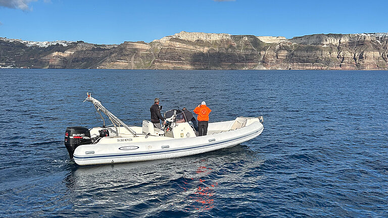 Drei Personen auf einem motorgetriebenen Schlauchboot, eine Frau schaut durch ein Fernglas, eine Person beugt sich über den Rand des Bootes ins Wasser