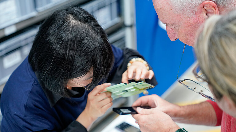 A young woman is showing an elderly couple a small folding microscope
