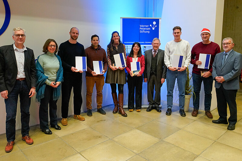 A group of people are standing in a lecture hall, six of them holding certificates in their hands.
