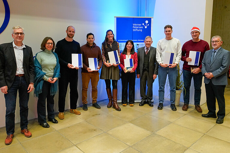 A group of people are standing in a lecture hall, six of them holding certificates in their hands.