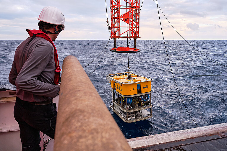  A yellow underwater robot is lowered into the water from the ship’s deck