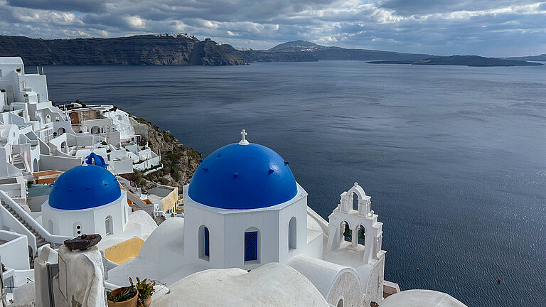 Weiß gekalkte Häuser mit leuchtend blauen Kuppeldächern am Rand einer steil abfallenden Küste