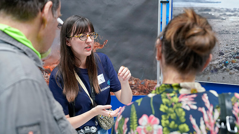 A young woman in a blue T-shirt is talking to an elderly couple, gesturing as she speaks