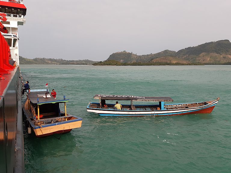 Zwei Holzboote nahe der Küste machen an einem großen Forschungsschiff fest