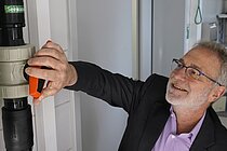 Ein Mann in lila Hemd und Anzugjacke dreht einen großen roten Hahn auf