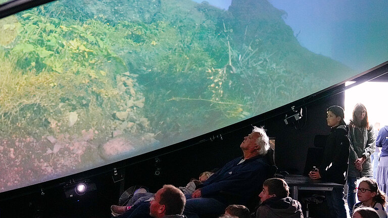 People are sitting and lying under a dome-shaped projection screen