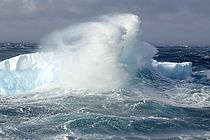 Eine Welle lässt Gischt an einem Eisberg hochspritzen.