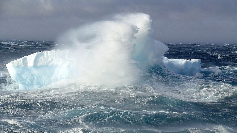 A wave causes spray to splash onto an iceberg.