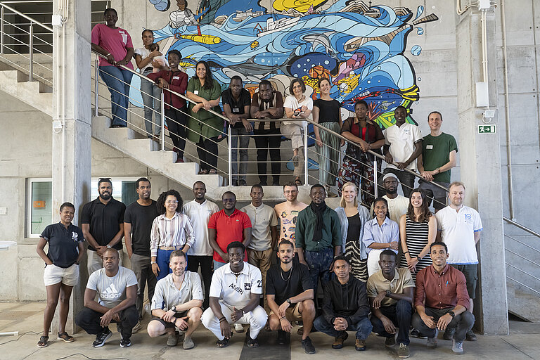 A group of dark-skinned people and a few light-skinned people are standing together and looking at the camera