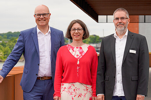 Two men and a woman stand on a roof terrace and look into the camera