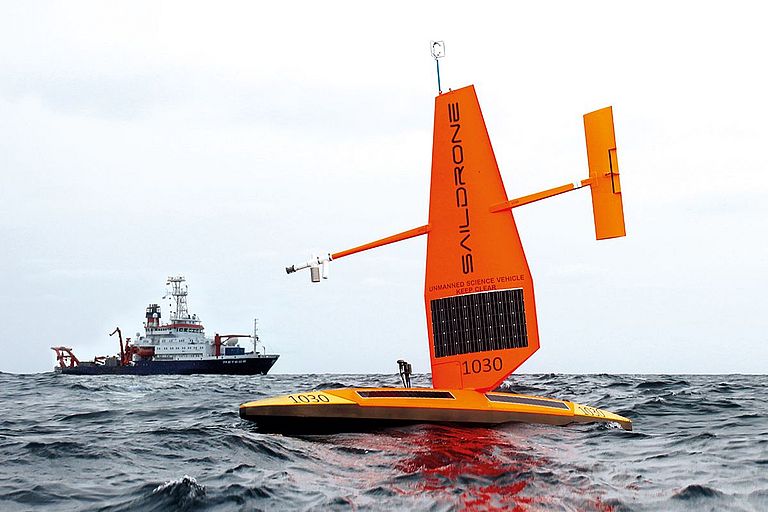 Eine orange Saildrone und das Forschungsschiff METEOR im Hintergrund. Foto: Arne Körtzinger/GEOMAR