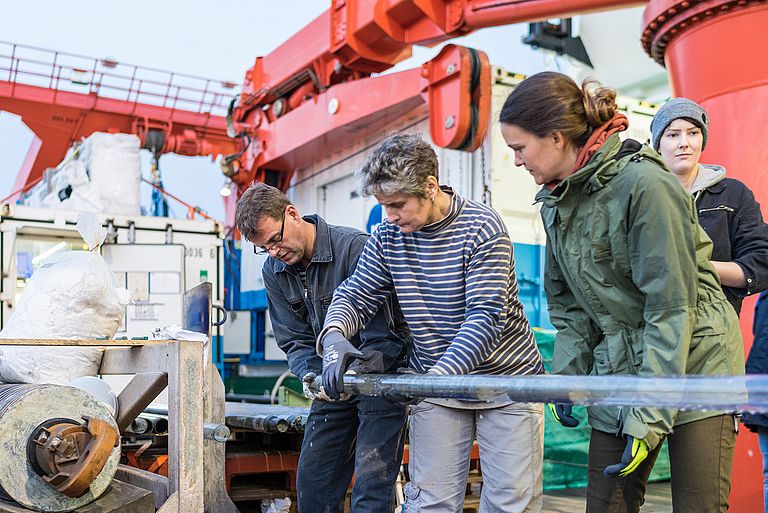 Researchers with a sediment core on board a research vessel
