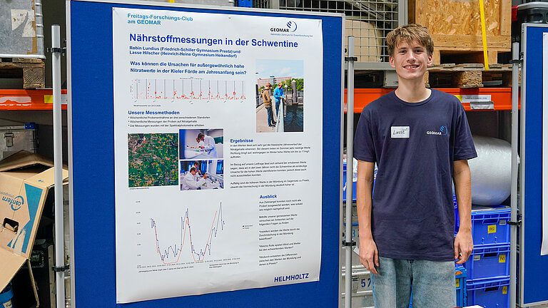 A young man is standing next to a poster display and smiling at the camera